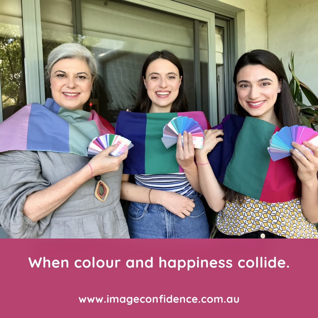 A mother and her two daughters are smiling. They are draped in their best colours and are each holding their perfect colour palette.