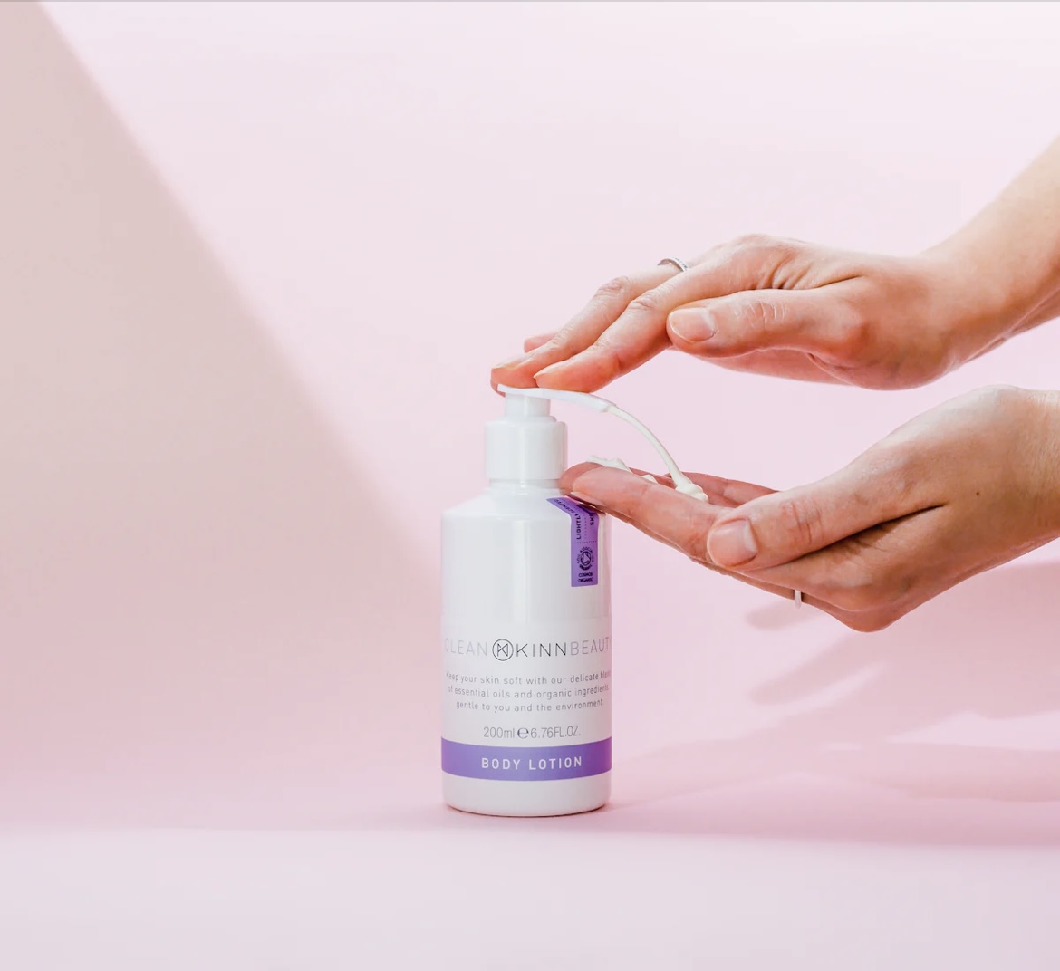 A woman's hands are shown pumping body lotion from a white container.