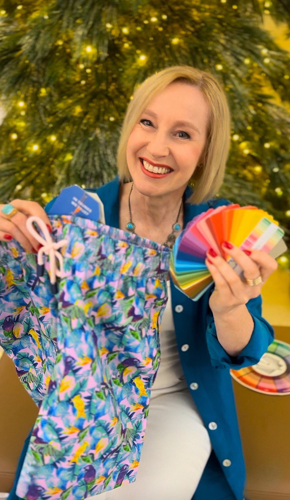 Ann Vodicka, Personal colour analysis expert, is smiling whilst holding a pair of vibrant boardshorts in one hand, and a Spicy colour swatch in the other.